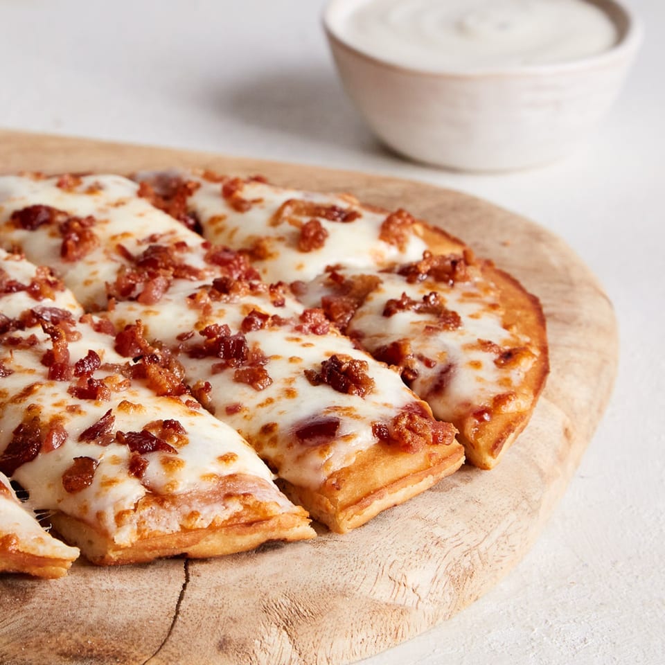 Oath Pizza's bacon and cheese pizza, sliced on a wooden board, with a side of dipping sauce.