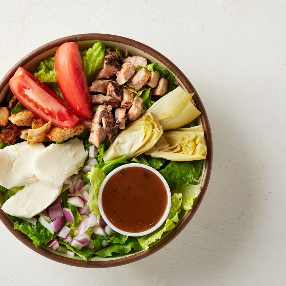 Oath Pizza salad with chicken, tomatoes, mozzarella, artichokes, red onion, croutons, and dressing.